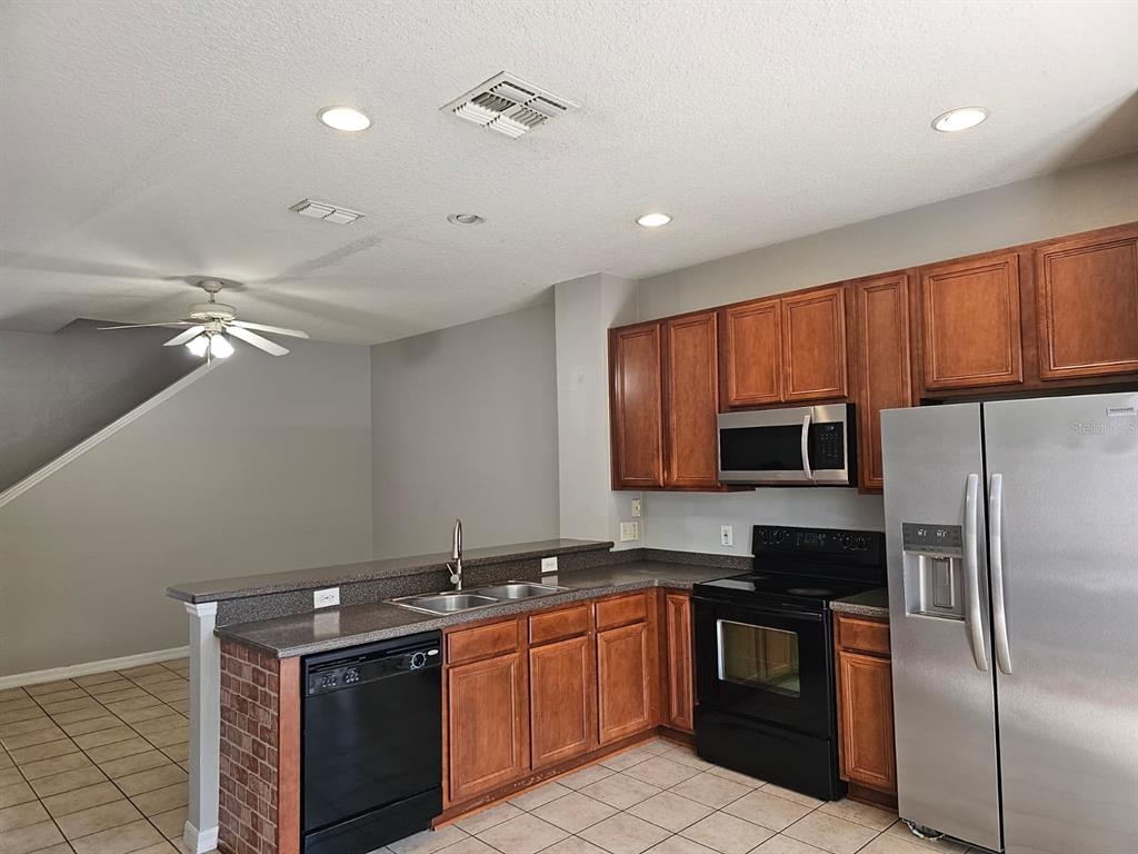 A kitchen features wood cabinets, stainless steel appliances, a brick-accented peninsula, and tile flooring — 5116 DOMINICA DRIVE, KISSIMMEE, FL