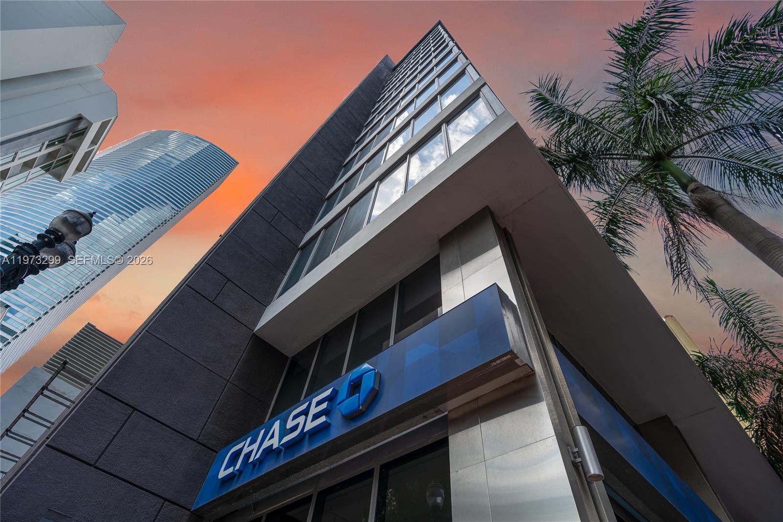 A low-angle view of a modern building exterior featuring a Chase bank sign and palm tree — 150 SE 2nd Ave # 1401, Miami FL 33131, MIAMI, FL