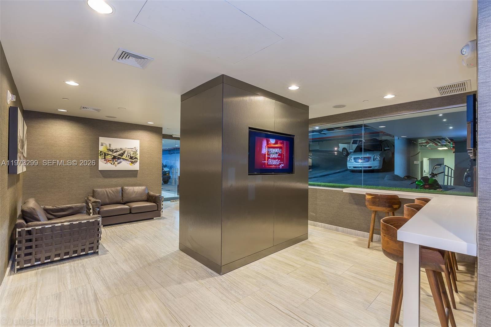 A modern lounge area features a central television pillar, leather seating, and a windowed wall — 150 SE 2nd Ave # 1401, Miami FL 33131, MIAMI, FL