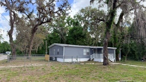 A gray manufactured home sits on a grassy lot surrounded by large, moss-covered trees — 10920-10928 MALATI STREET, NEW PORT RICHEY, FL