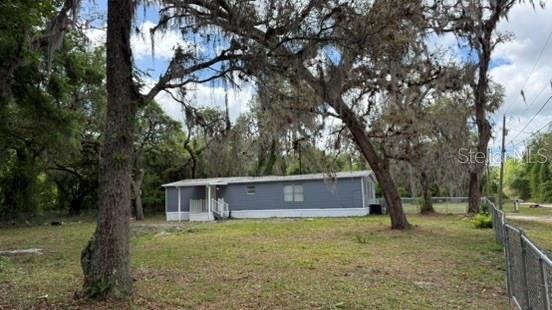 A grey manufactured home sits on a grassy lot surrounded by large, moss-covered oak trees — 10920-10928 MALATI STREET, NEW PORT RICHEY, FL