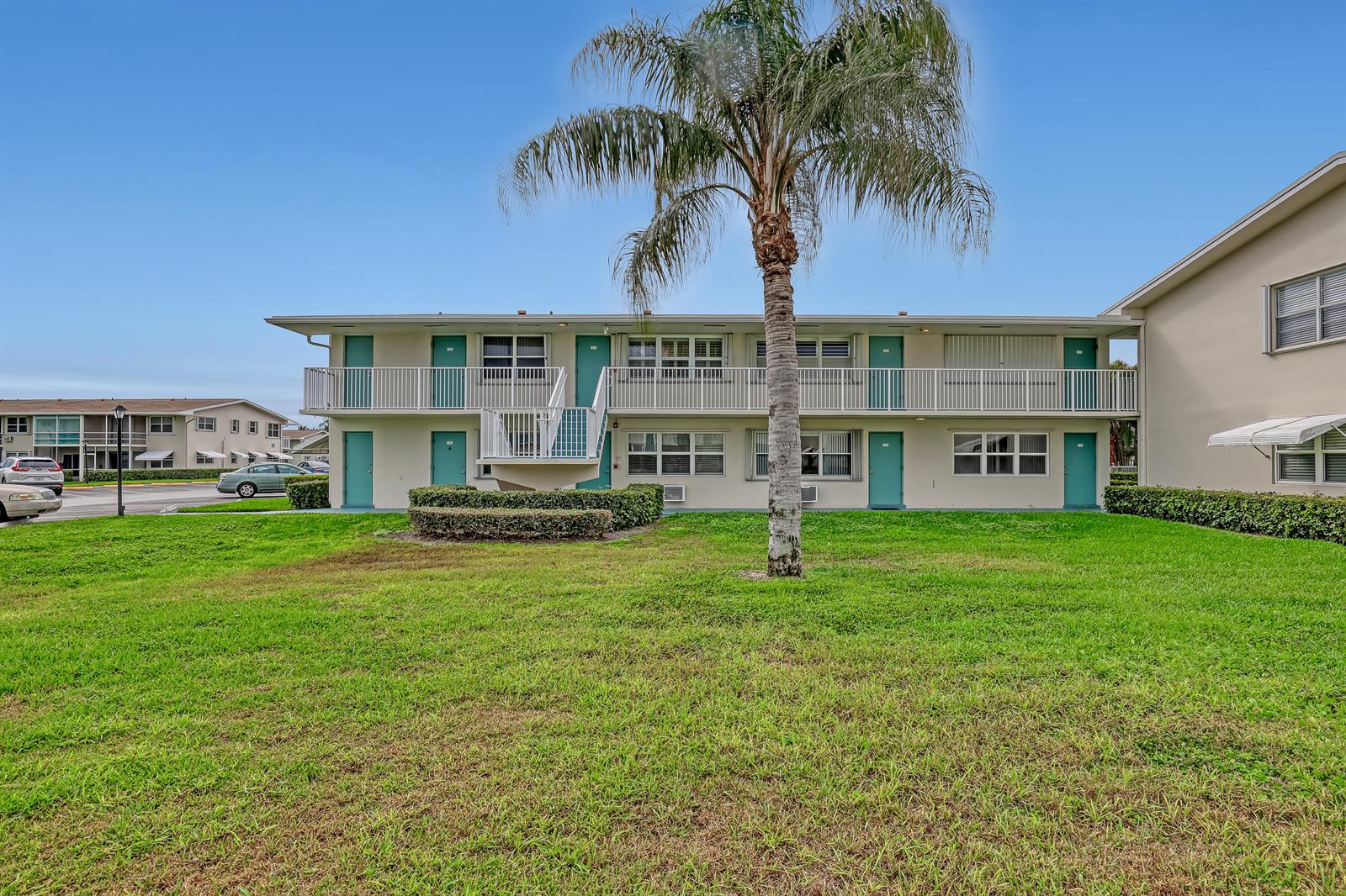 A two-story apartment building features teal doors, white railings, and a central palm tree — 680 Horizon W # 110, Boynton Beach FL 33435, BOYNTON BEACH, FL