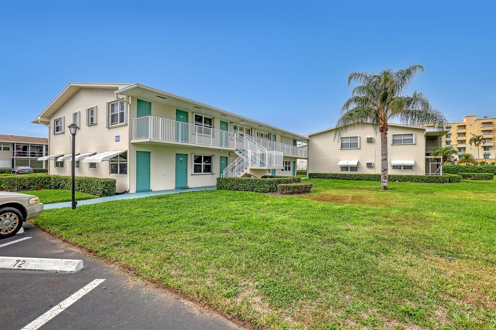 Two-story apartment buildings with teal doors and white balconies sit on a grassy lot — 680 Horizon W # 110, Boynton Beach FL 33435, BOYNTON BEACH, FL