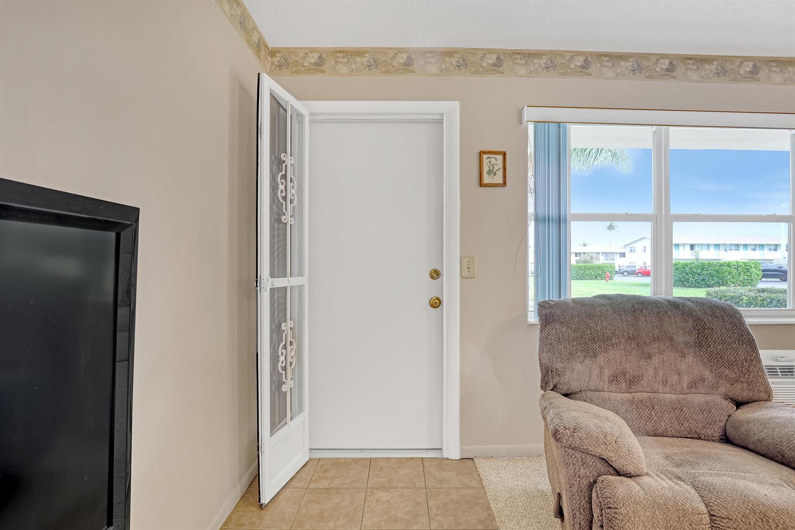 A living room features a white door with a screen, tile flooring, and a recliner — 680 Horizon W # 110, Boynton Beach FL 33435, BOYNTON BEACH, FL