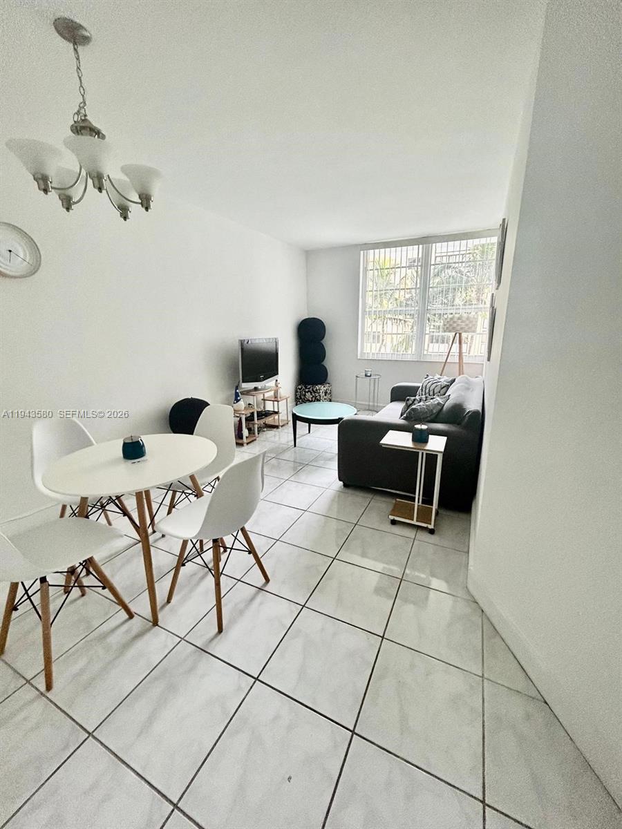 A living and dining area features white tile floors, a chandelier, and a gray sofa — 100 Lincoln Rd # 524, Miami Beach FL 33139, MIAMI BEACH, FL