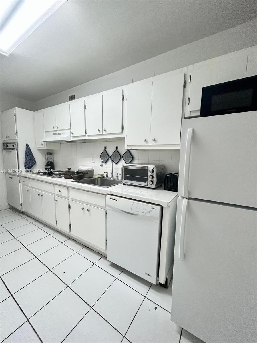 A white kitchen features tiled floors, white cabinetry, a dishwasher, and a refrigerator — 100 Lincoln Rd # 524, Miami Beach FL 33139, MIAMI BEACH, FL