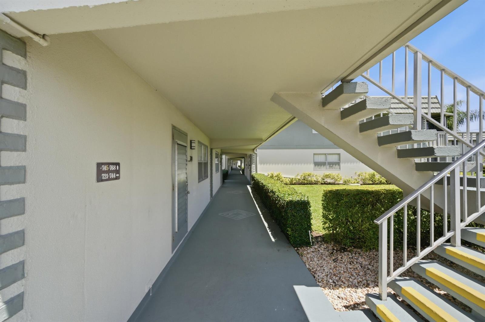 An outdoor apartment walkway features a staircase, a hedge, and unit number signage — 724 Flanders P, Delray Beach FL 33484, DELRAY BEACH, FL