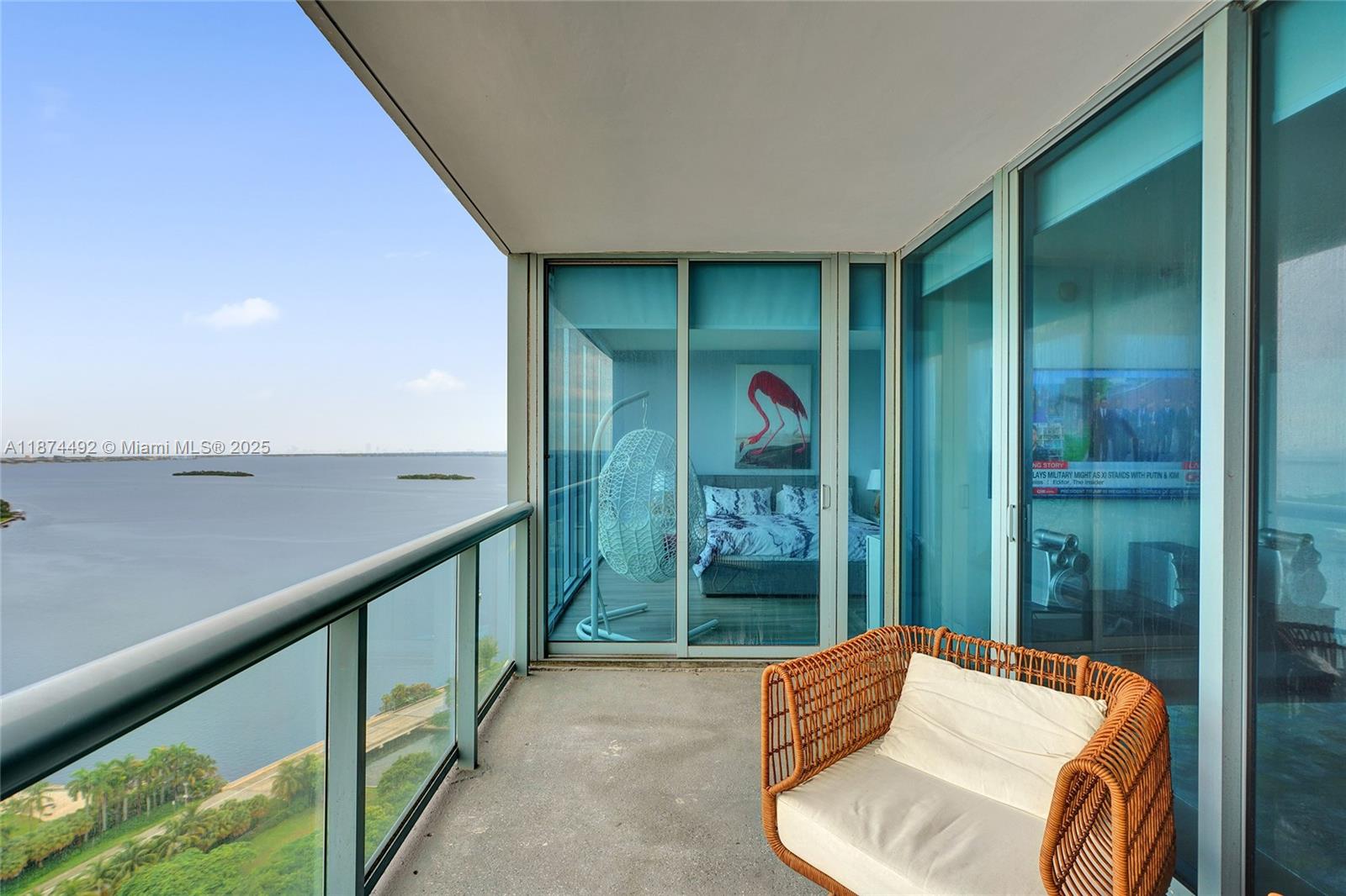 A balcony with a wicker chair overlooks a body of water and a bedroom — 601 NE 36th St # 2703, Miami FL 33137, MIAMI, FL
