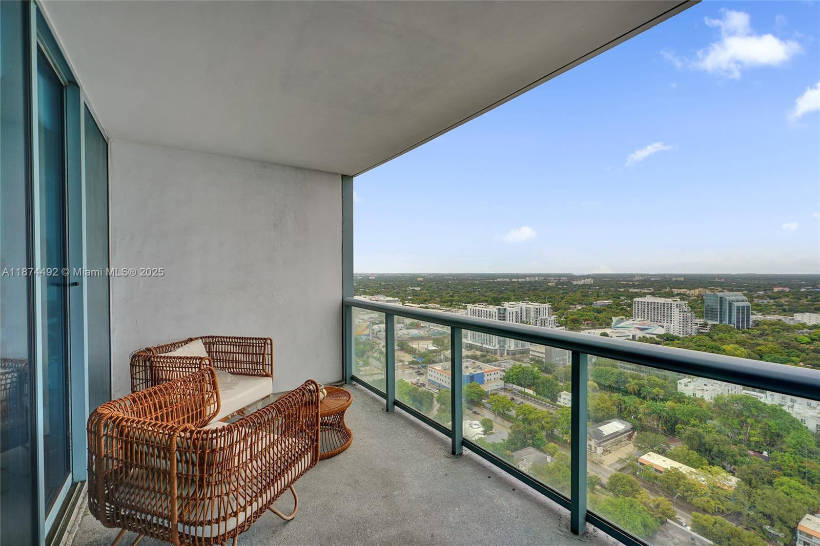 A high-rise balcony features two wicker chairs and a small table overlooking a city view — 601 NE 36th St # 2703, Miami FL 33137, MIAMI, FL