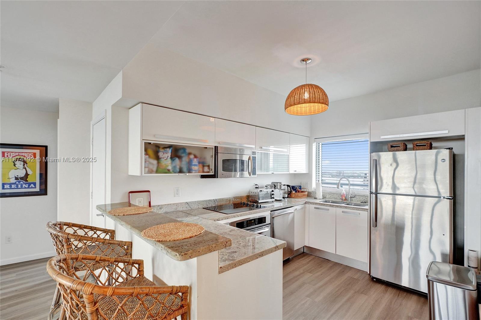 A kitchen features white cabinets, stainless steel appliances, a granite breakfast bar, and wicker stools — 601 NE 36th St # 2703, Miami FL 33137, MIAMI, FL