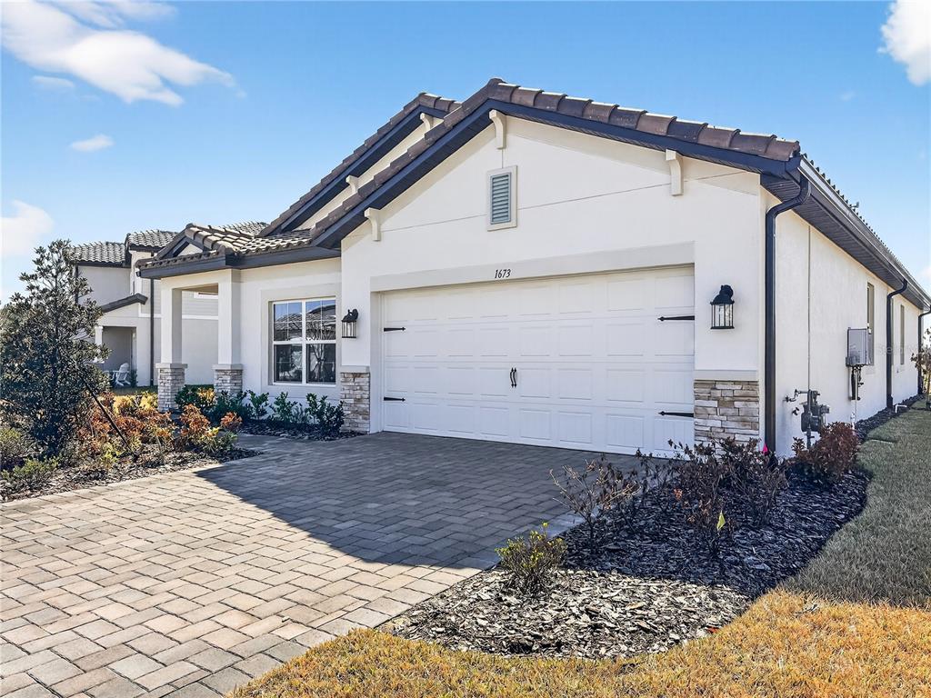 A single-story house with a white stucco exterior, a two-car garage, and a paver driveway — 1673 SUTTONSET TRAIL, ZEPHYRHILLS, FL