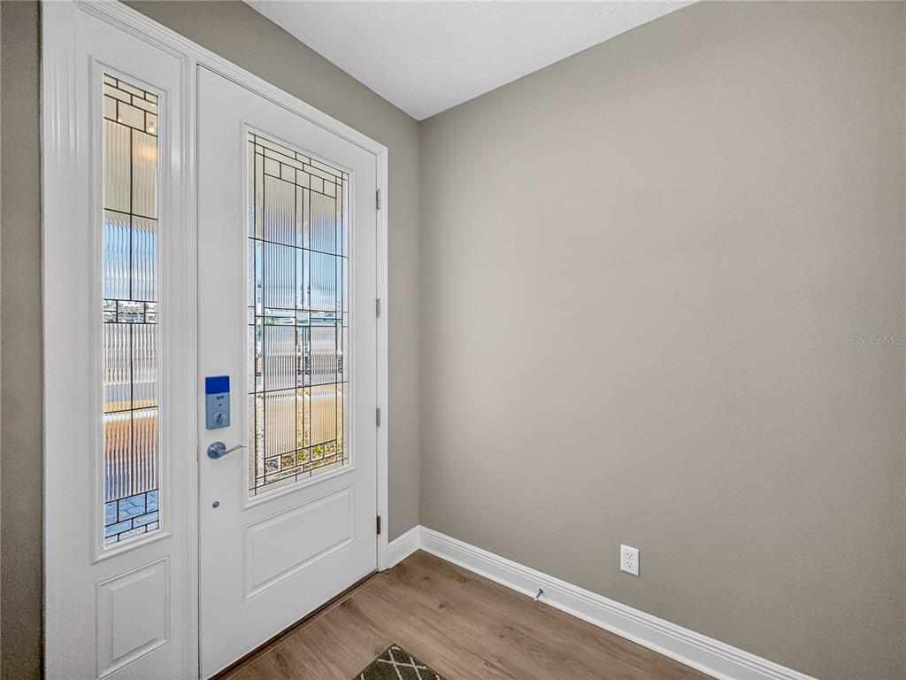 An entryway features a white front door with decorative glass panels, gray walls, and wood-look flooring — 1673 SUTTONSET TRAIL, ZEPHYRHILLS, FL