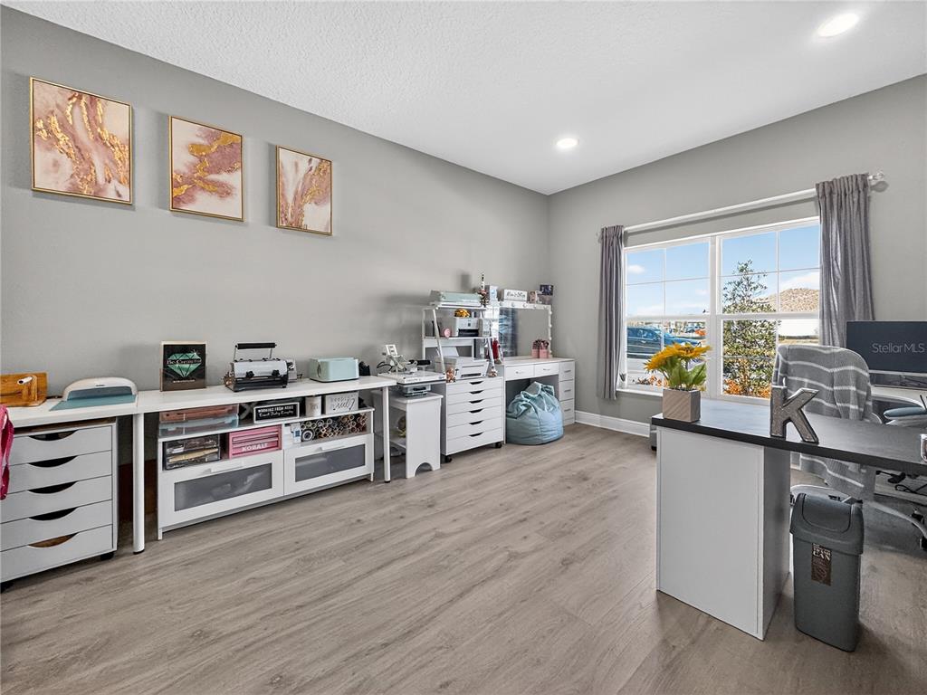 A craft room features a desk, storage cabinets, wall art, and a window with gray curtains — 1673 SUTTONSET TRAIL, ZEPHYRHILLS, FL