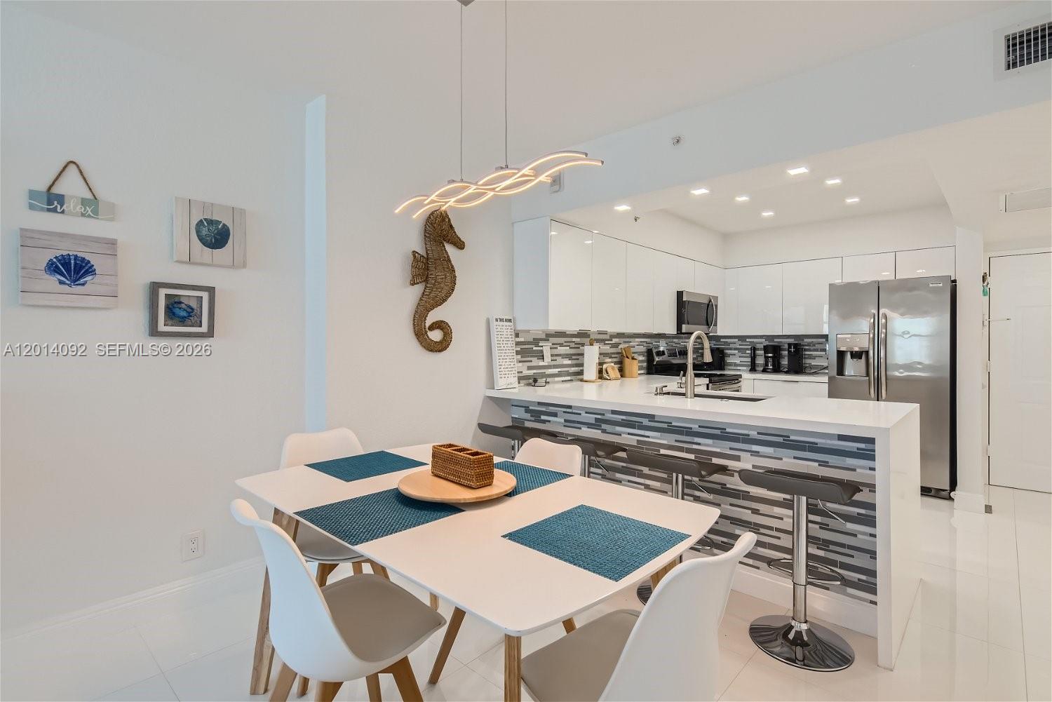 A dining area with a white table sits adjacent to a modern kitchen with bar seating — 2501 S Ocean Dr # 1103, Hollywood FL 33019, HOLLYWOOD, FL