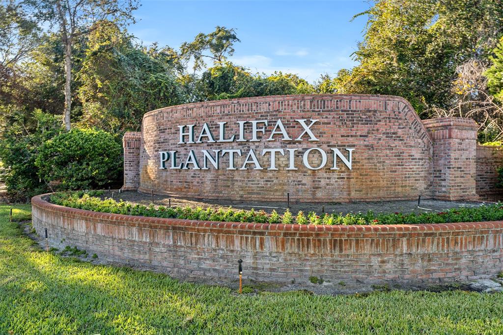 A brick monument sign displays the words Halifax Plantation in a landscaped garden setting — 3040 ACOMA DRIVE, ORMOND BEACH, FL