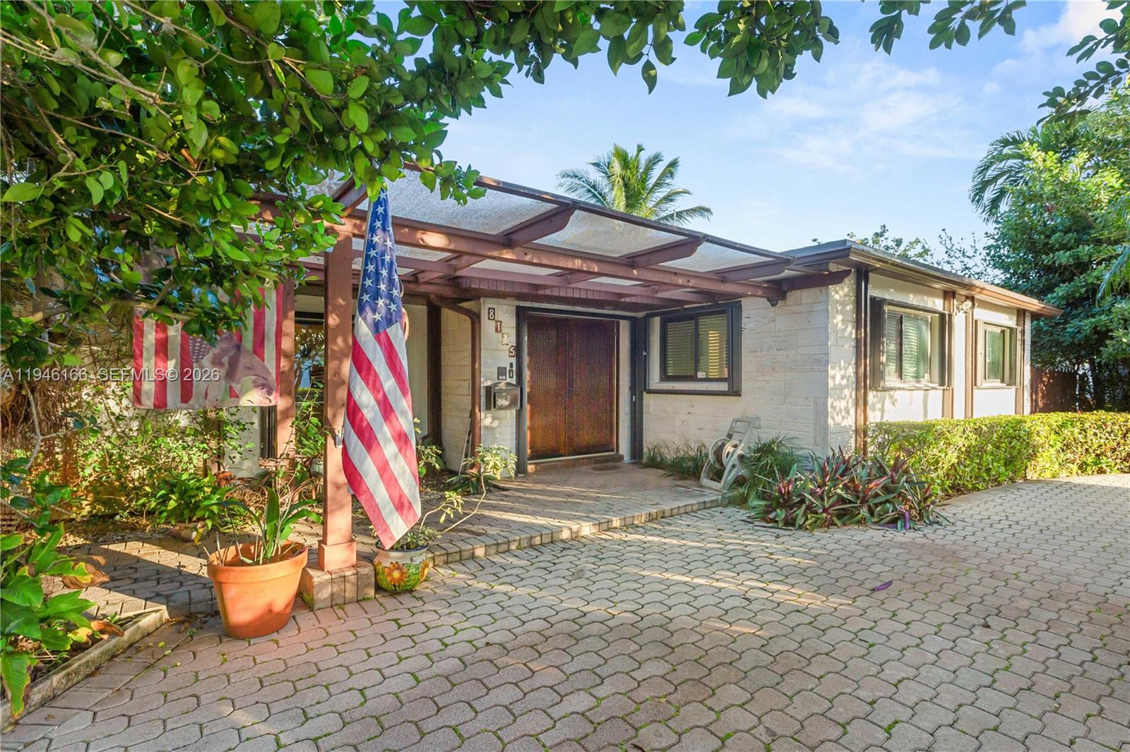 A single-story house features a paved driveway, a covered entryway, and an American flag — 8115 SW 92nd Ct, Miami FL 33173, MIAMI, FL