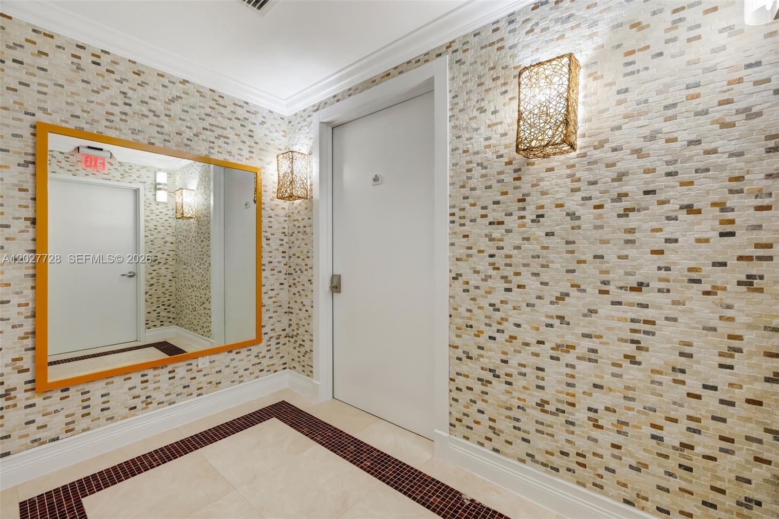 An indoor entryway features a white door, a large mirror, and walls with textured tiles — 50 S Pointe Dr # 903, Miami Beach FL 33139, MIAMI BEACH, FL