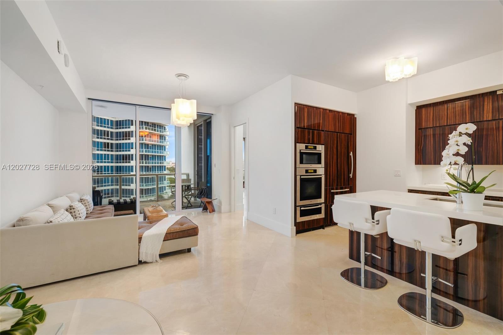 A modern open-concept living area features a kitchen with wood cabinetry and a white sofa — 50 S Pointe Dr # 903, Miami Beach FL 33139, MIAMI BEACH, FL