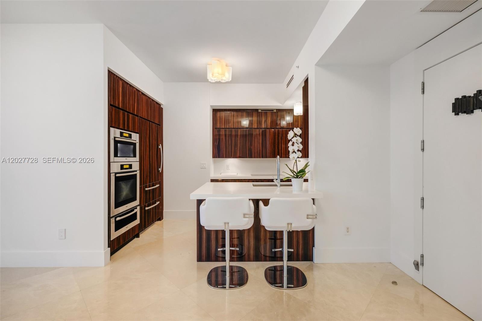 A modern kitchen features dark wood cabinetry, stainless steel appliances, and a white breakfast bar — 50 S Pointe Dr # 903, Miami Beach FL 33139, MIAMI BEACH, FL