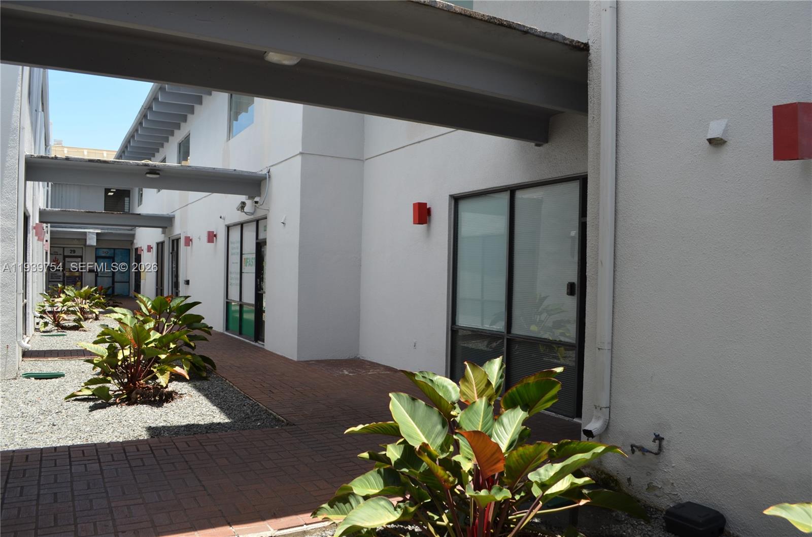 A paved walkway leads between two white buildings with large windows and potted plants — 7311 NW 12th St # 20, Miami FL 33126, MIAMI, FL