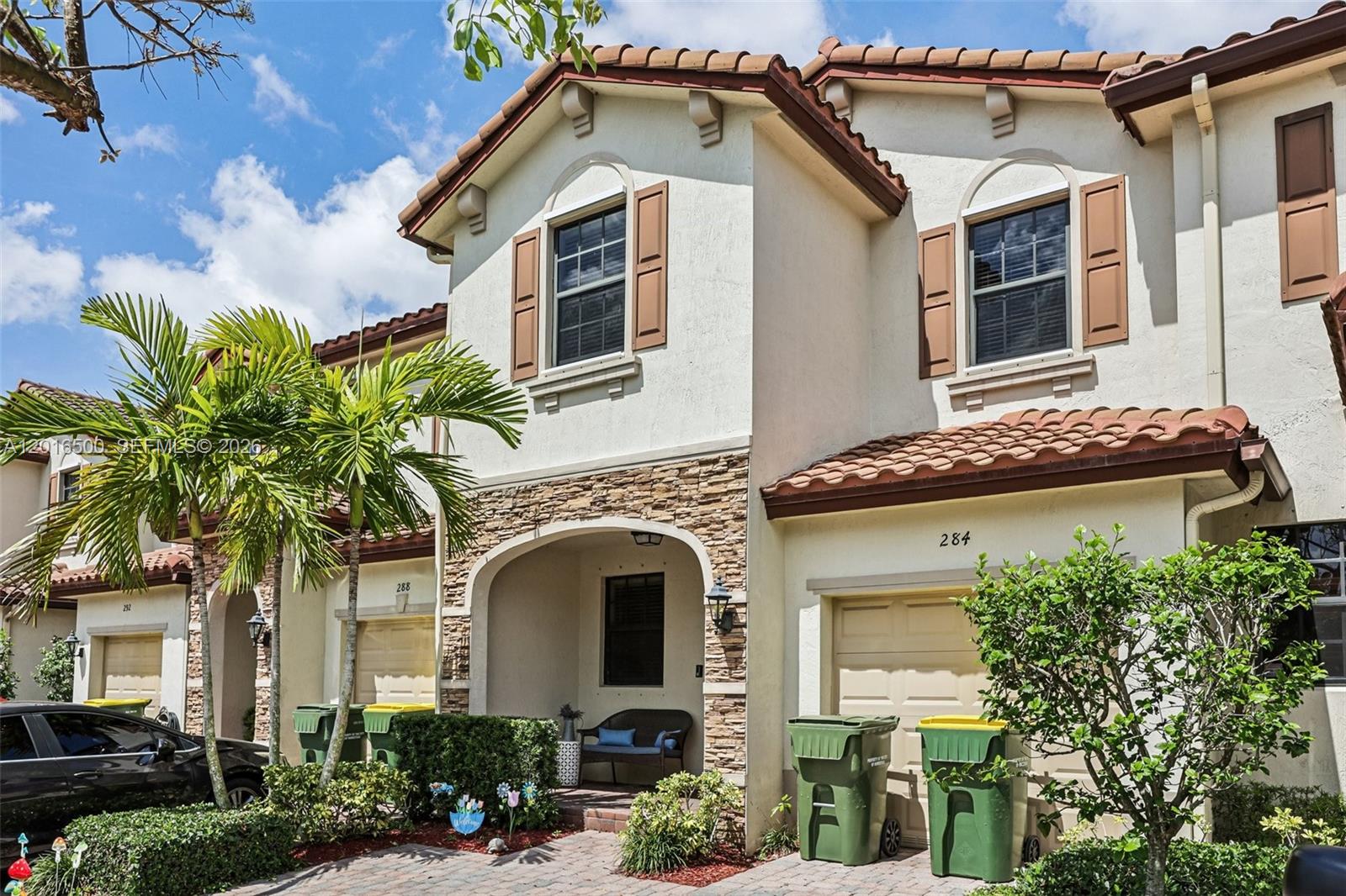 A multi-story townhouse exterior features stucco walls, stone accents, a tiled roof, and garage doors — 284 SE 37th Ter, Homestead FL 33033, HOMESTEAD, FL