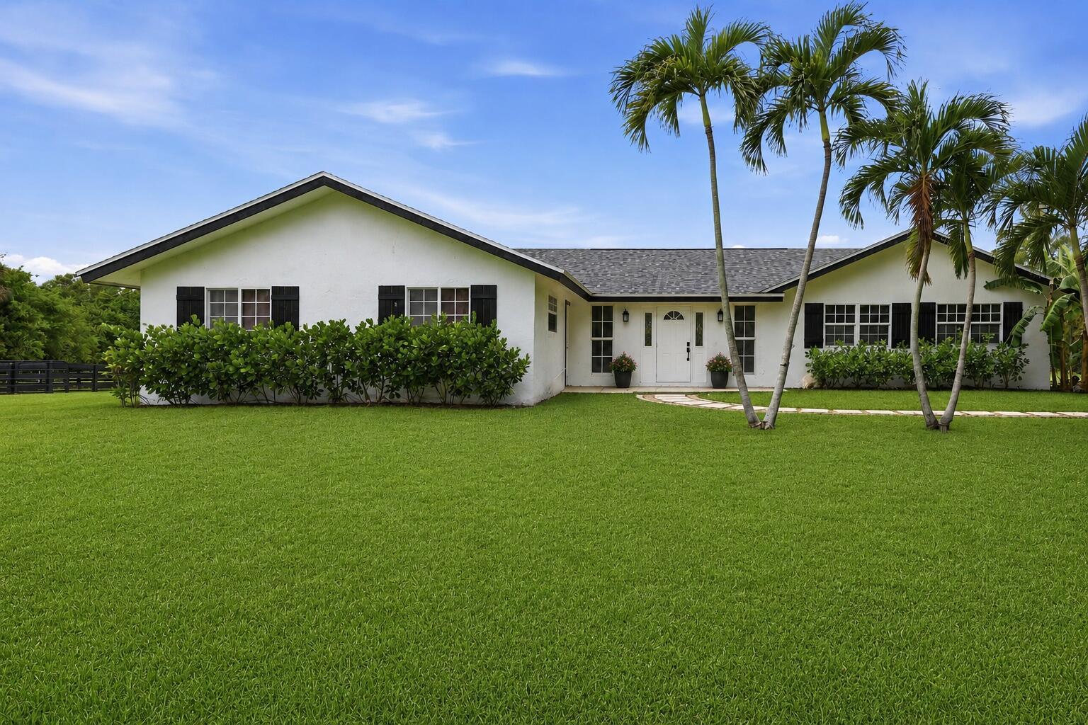 A single-story white house with black shutters and palm trees sits behind a large lawn — 785 Cindy Drive, Wellington FL 33414, WELLINGTON, FL