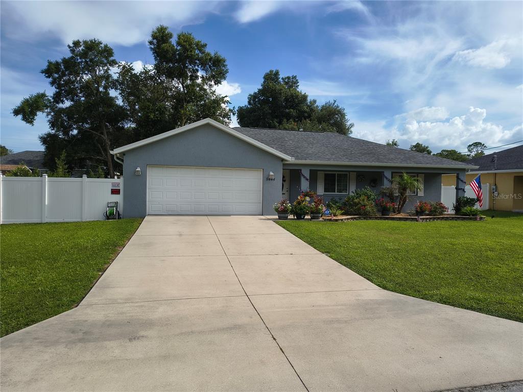 A gray, single-story house with a two-car garage and a front porch sits on grass — 9444 SE 161ST STREET, SUMMERFIELD, FL