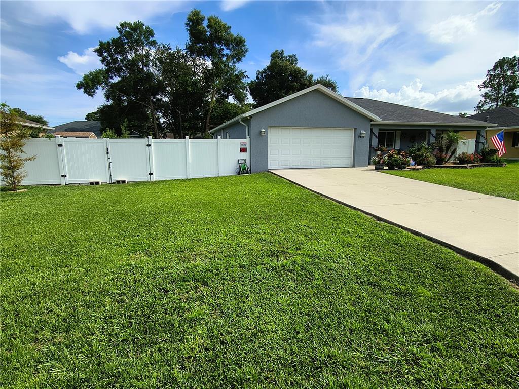 A gray single-story house features a covered front porch, landscaping, and a stone retaining wall — 9444 SE 161ST STREET, SUMMERFIELD, FL