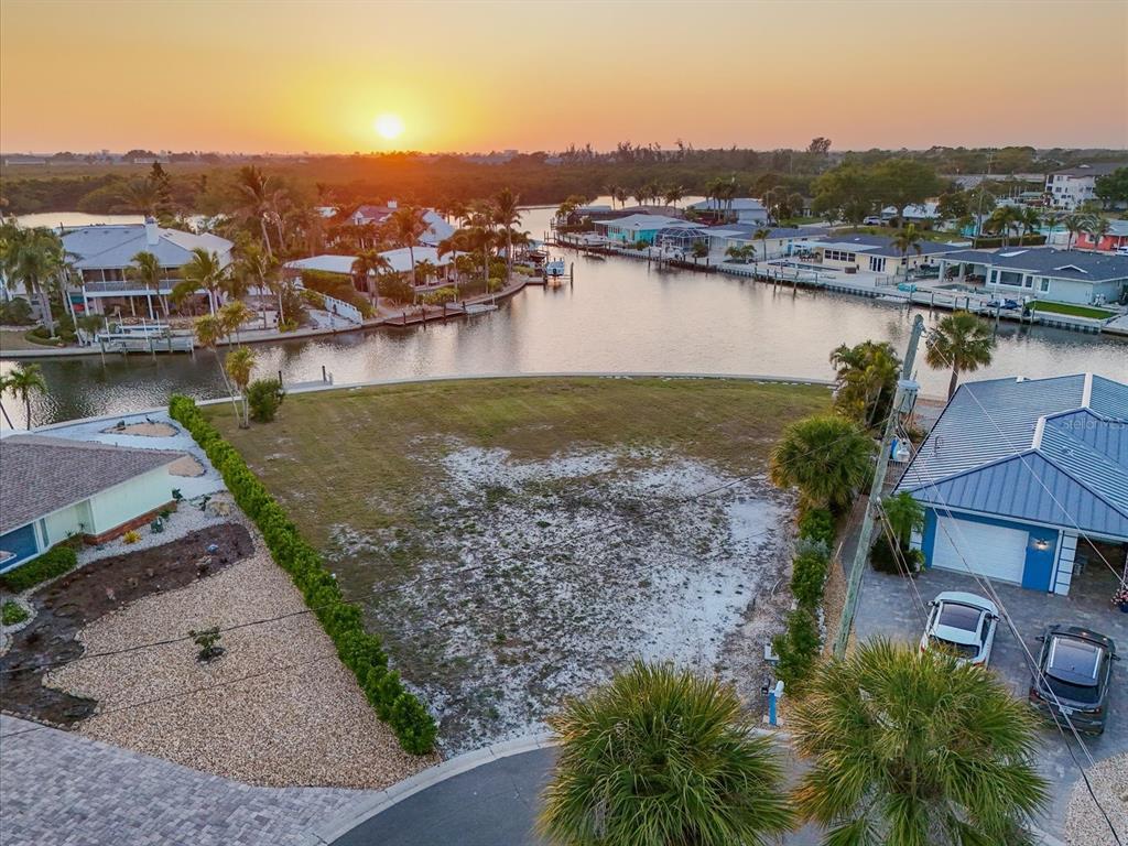 An aerial view shows a vacant waterfront lot situated between two houses at sunset — 10412 KINGFISHER ROAD W, BRADENTON, FL