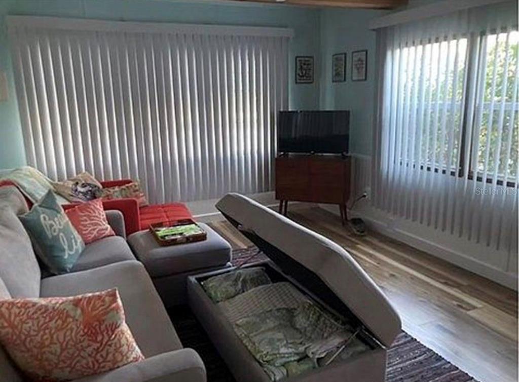 A living room features a gray sectional sofa, a storage ottoman, and vertical window blinds — 3721 116TH STREET W, BRADENTON, FL