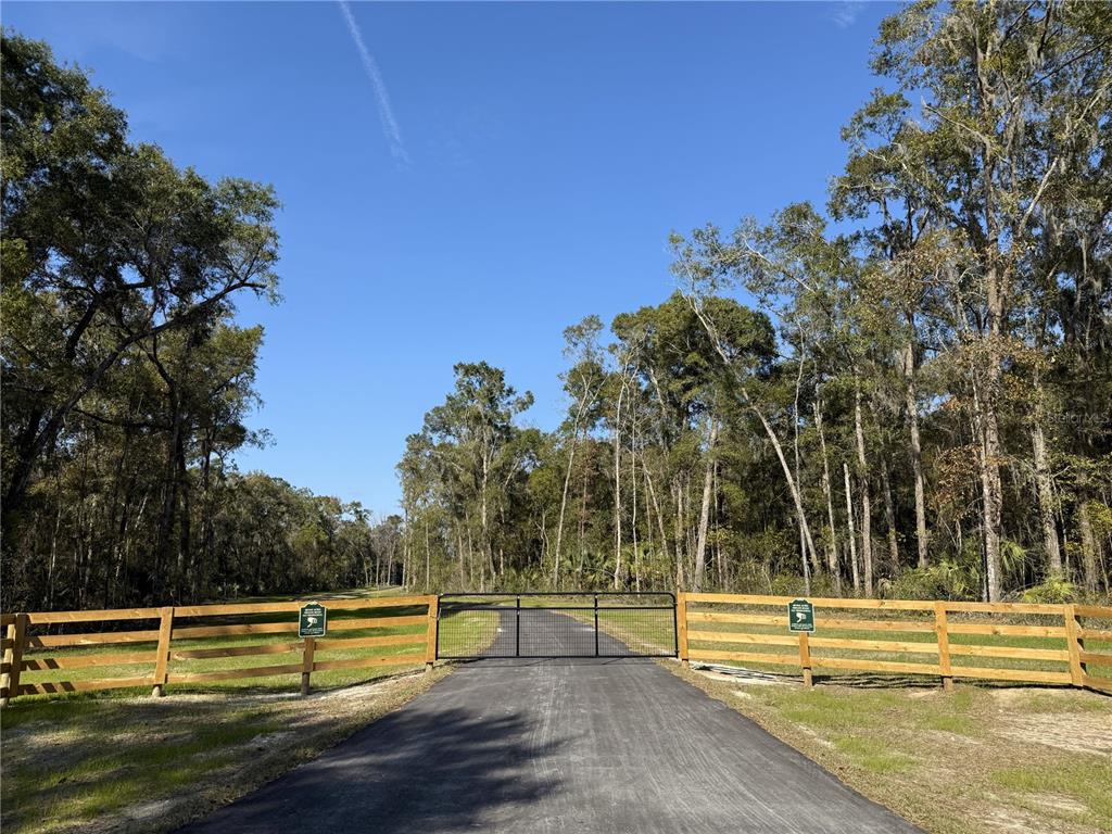 A paved driveway leads to a black metal gate flanked by wooden rail fencing — Irvine Acres #3 (10ac) W HWY 318, REDDICK, FL