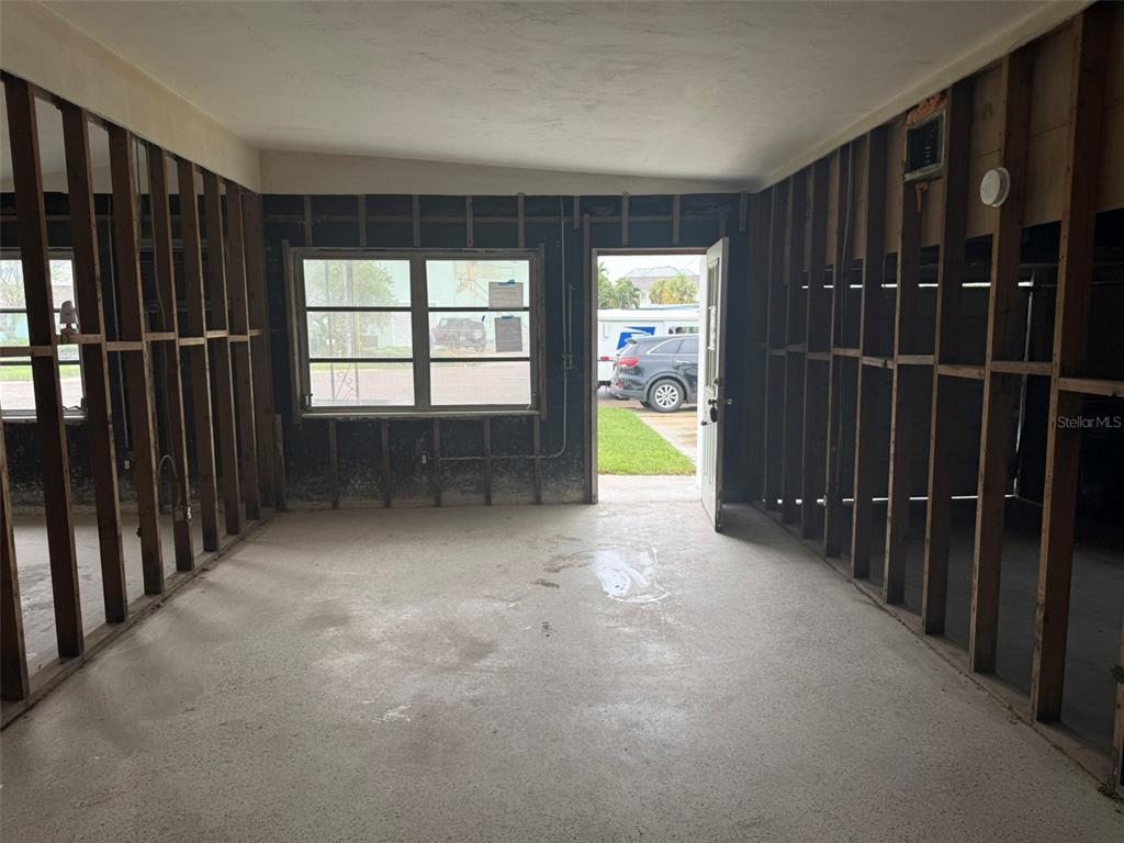 An unfinished room with exposed wall studs, a concrete floor, a window, and an open door — 14054 VIVIAN DRIVE, MADEIRA BEACH, FL
