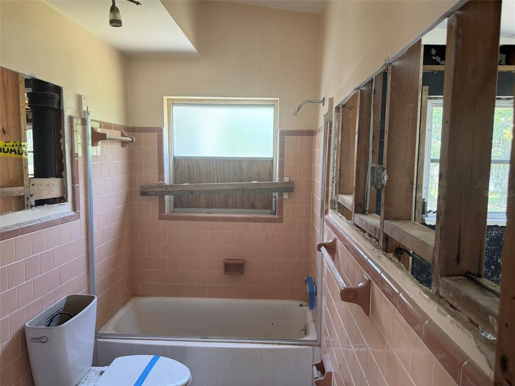 A bathroom undergoing renovation features pink wall tiles, a bathtub, and exposed wooden wall studs — 14054 VIVIAN DRIVE, MADEIRA BEACH, FL