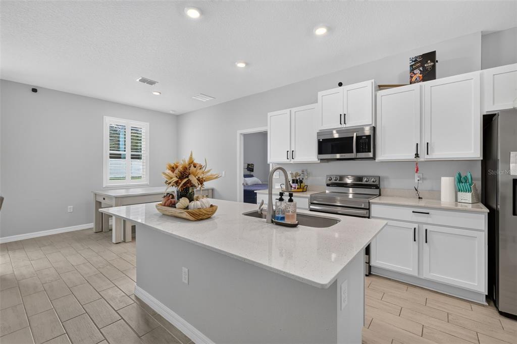 A kitchen with white cabinets, a quartz-topped island, stainless steel appliances, and light tile flooring — 149 MARION OAKS GOLF ROAD, OCALA, FL