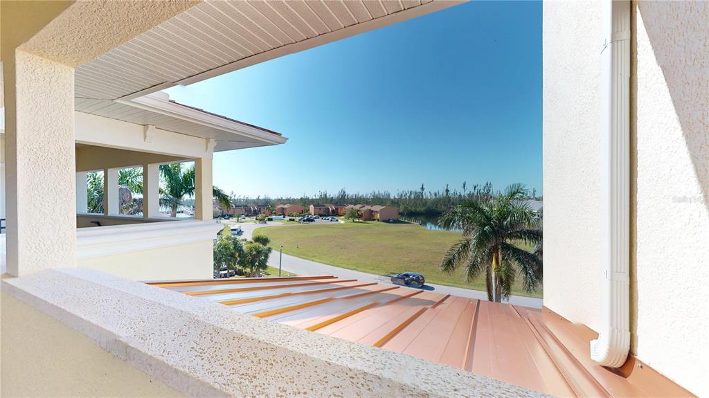 A view from a balcony overlooking a metal roof, a grassy field, and distant buildings — 1340 ROCK DOVE COURT UNIT 143, PUNTA GORDA, FL