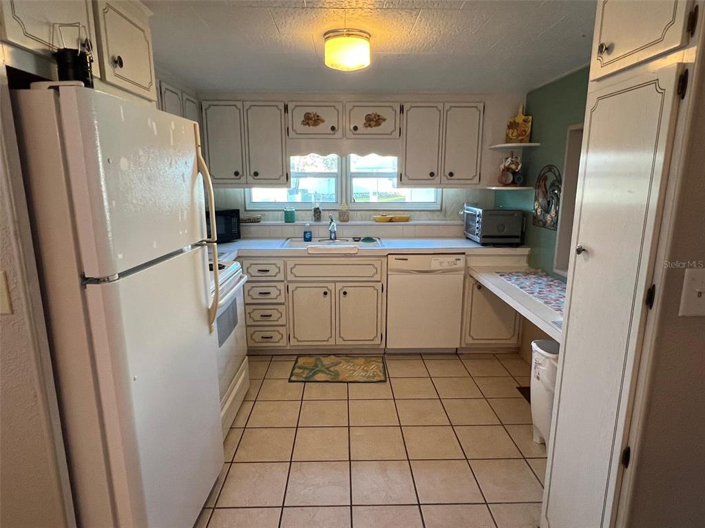 A kitchen features white cabinets, a white refrigerator, a dishwasher, and tiled flooring — 29250 US HIGHWAY 19 N UNIT 301, CLEARWATER, FL