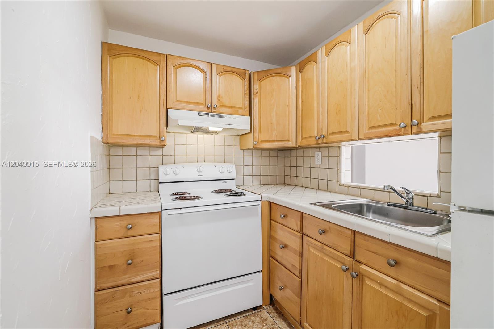 A kitchen features light wood cabinets, white appliances, tiled countertops, and a stainless steel sink — 6200 W Flagler St # 208, Miami FL 33144, MIAMI, FL