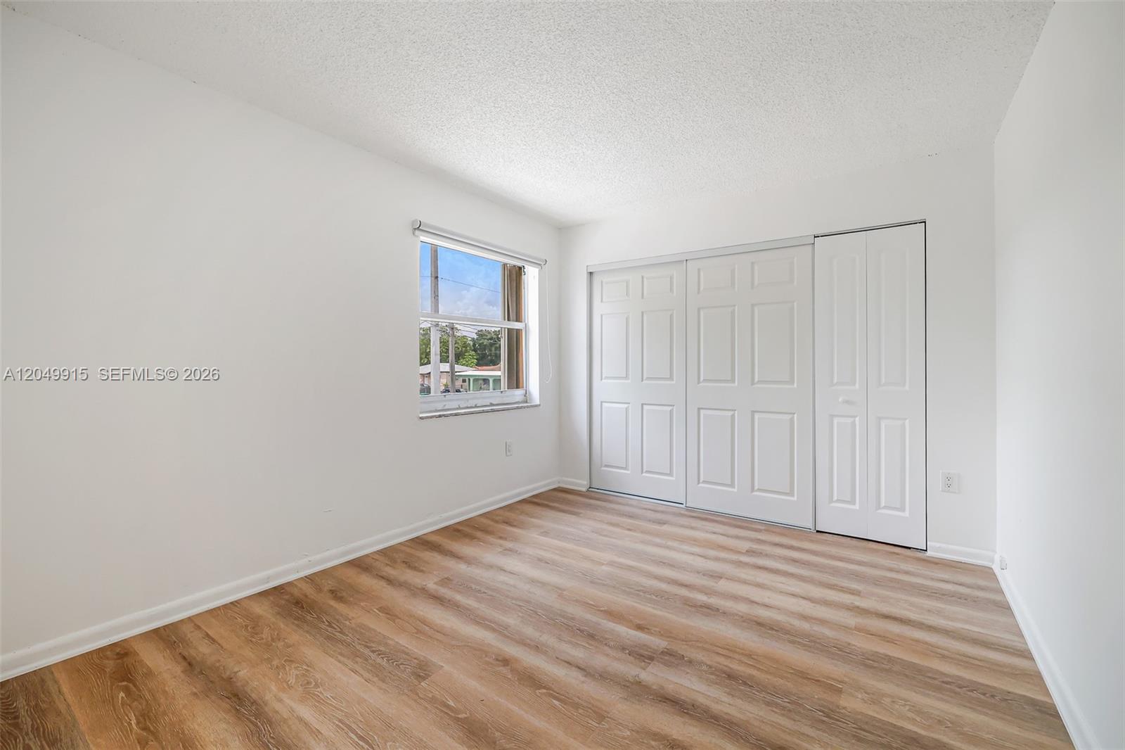An empty bedroom features white walls, wood-look flooring, a window, and white closet doors — 6200 W Flagler St # 208, Miami FL 33144, MIAMI, FL