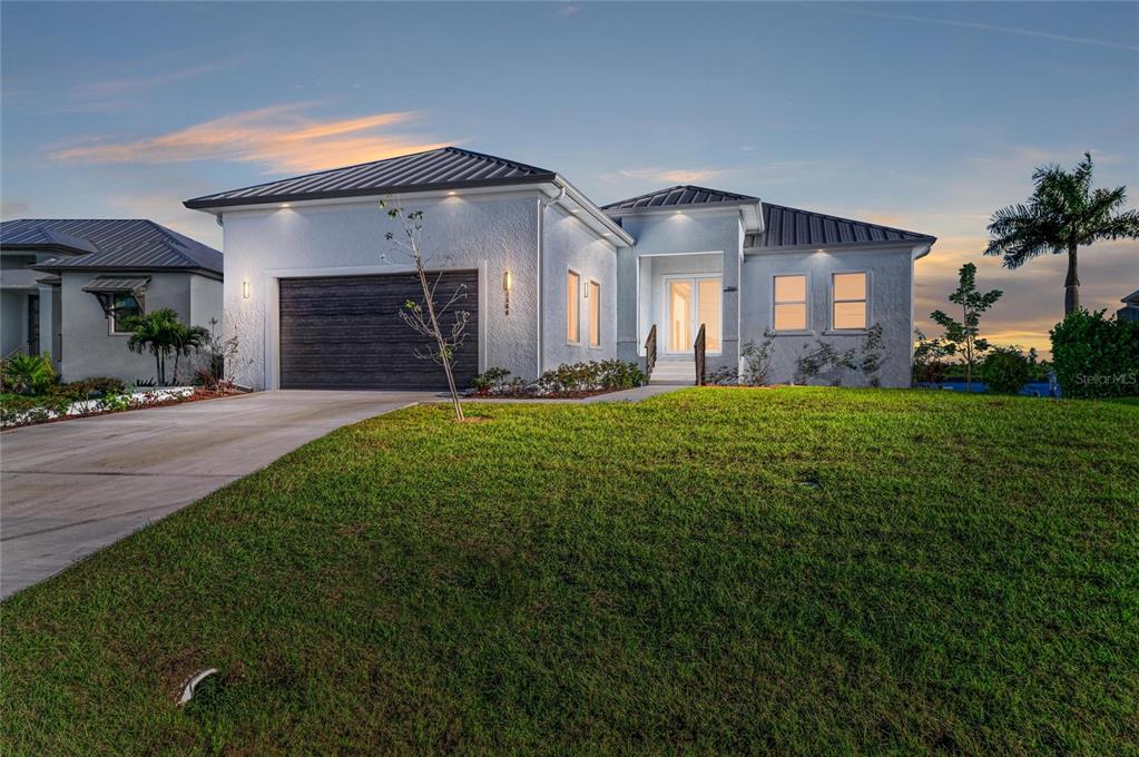 A modern, single-story house with a white stucco exterior, dark metal roof, and attached garage — 3564 PEACE RIVER DRIVE, PUNTA GORDA, FL