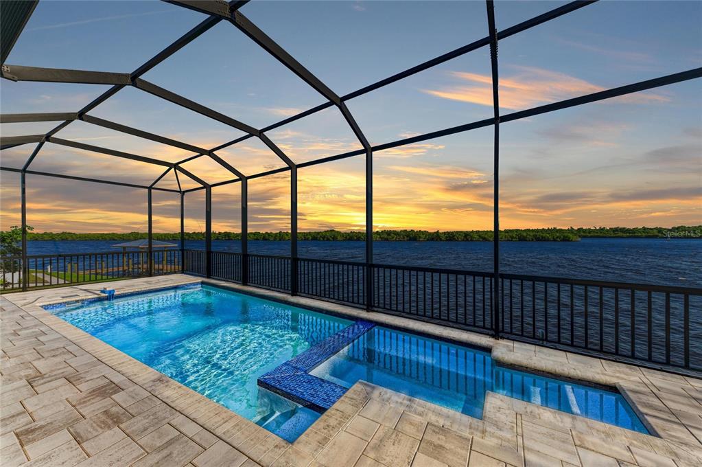 A screened-in pool and spa overlook a large body of water at sunset — 3564 PEACE RIVER DRIVE, PUNTA GORDA, FL
