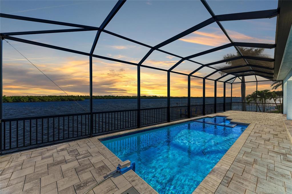 A screened-in pool patio overlooks a large body of water at sunset — 3564 PEACE RIVER DRIVE, PUNTA GORDA, FL