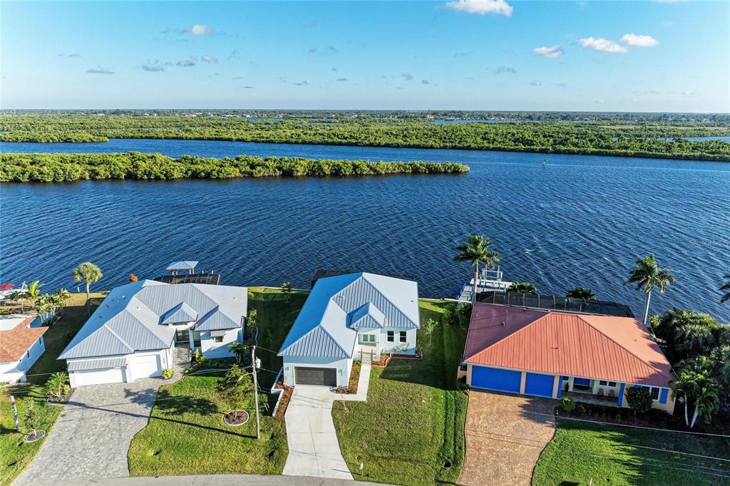 An aerial view shows three waterfront houses with metal roofs along a river — 3564 PEACE RIVER DRIVE, PUNTA GORDA, FL