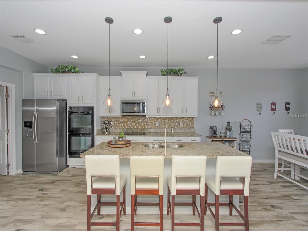 A kitchen features white cabinets, granite countertops, a central island with bar stools, and stainless appliances — 15214 GALBI DRIVE, ORLANDO, FL