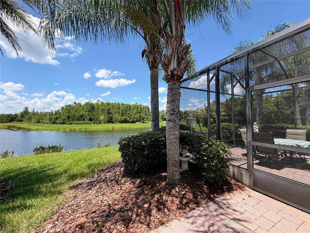 A screened-in patio overlooks a grassy lawn, a pond, and a line of trees — 106 PRIMA DRIVE, POINCIANA, FL