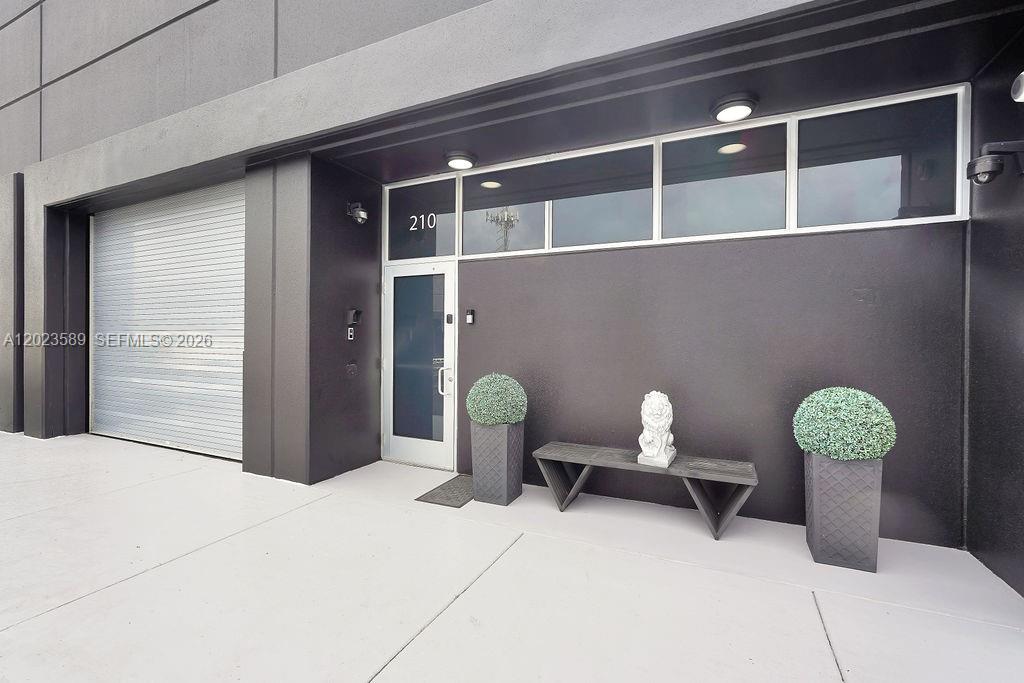 The exterior of a commercial building features a gray door, a roll-up gate, and planters — 6030 NW 102nd Ave # 210, Doral FL 33178, DORAL, FL