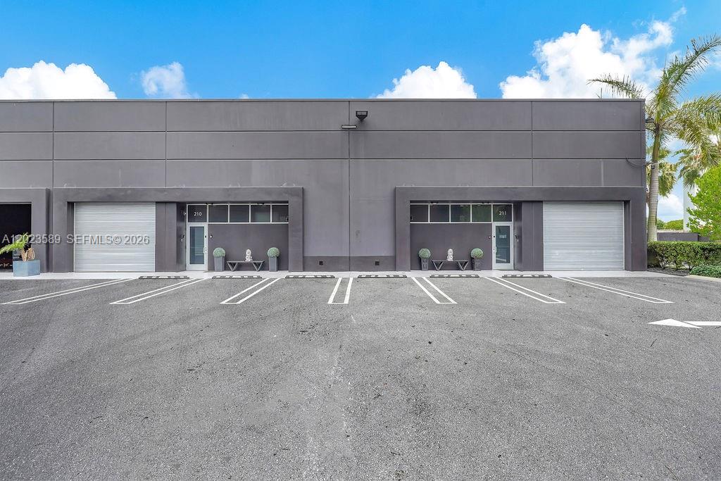 A modern commercial building exterior features two gray units with roll-up doors and glass entryways — 6030 NW 102nd Ave # 210, Doral FL 33178, DORAL, FL