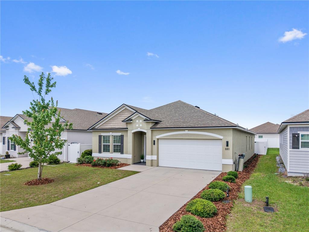 A single-story house with a white garage door, tan stucco exterior, and a concrete driveway — 880 NW 251ST DRIVE, NEWBERRY, FL