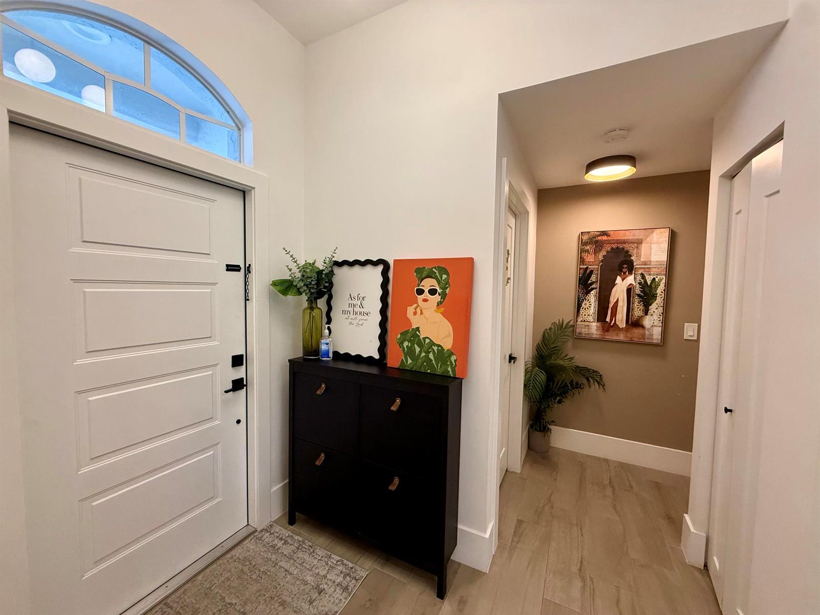 An entryway features a white door, a black shoe cabinet, and a hallway with artwork — 1073 Aspri Way, Riviera Beach FL 33418, RIVIERA BEACH, FL