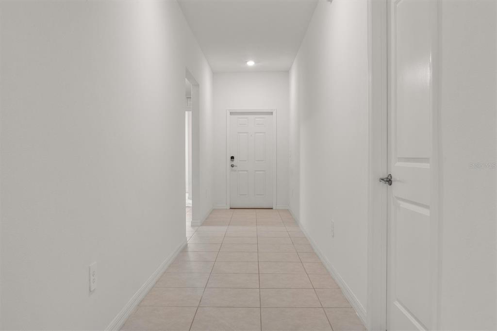 A bright, empty hallway with white walls, tiled flooring, and a white front door — 1856 RED LOOP, LAKELAND, FL