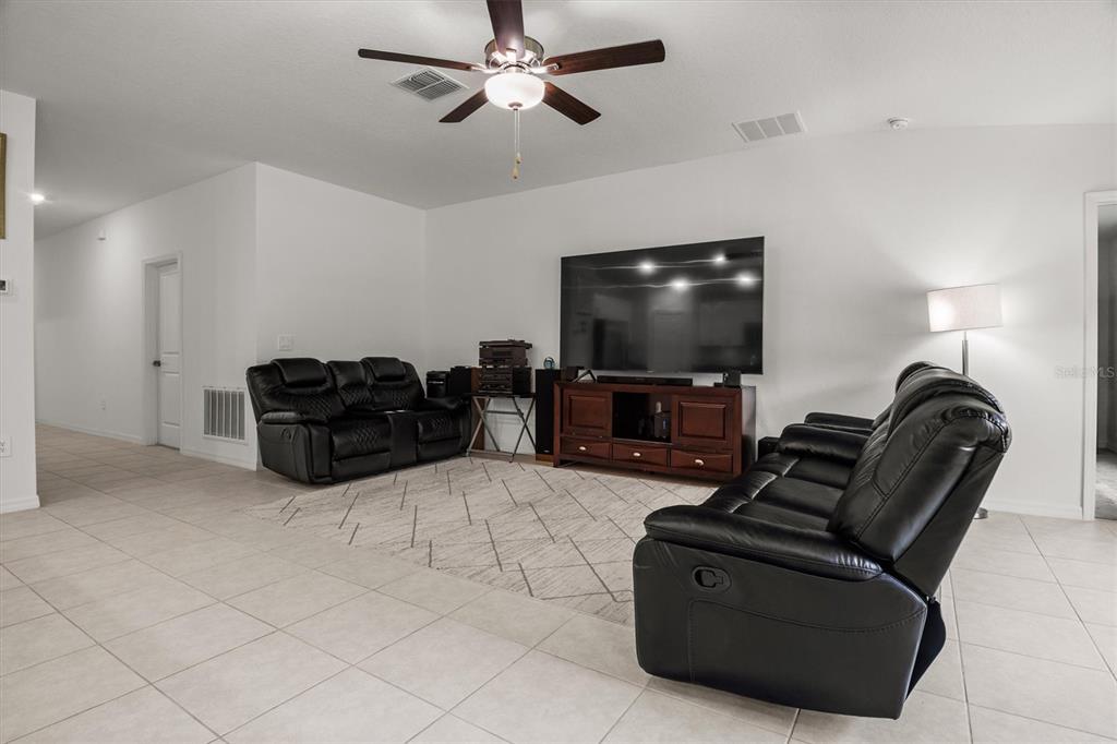 A living room features tile flooring, two black leather sofas, and a large television console — 1856 RED LOOP, LAKELAND, FL